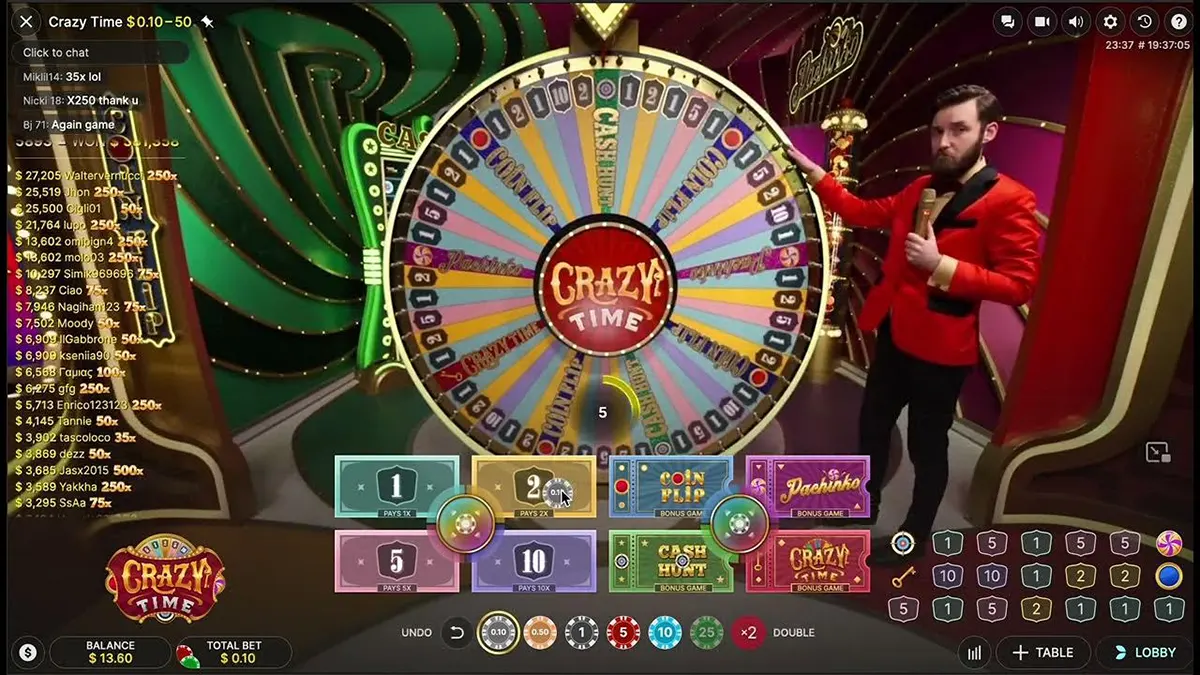 Screenshot of the Crazy Time live game showing a large colourful wheel in a studio set, with a male host in a red jacket holding a microphone, a chat and recent wins list on the left, and the betting interface at the bottom with options for 1–10 and bonus games like Coin Flip, Cash Hunt, Pachinko, and Crazy Time.